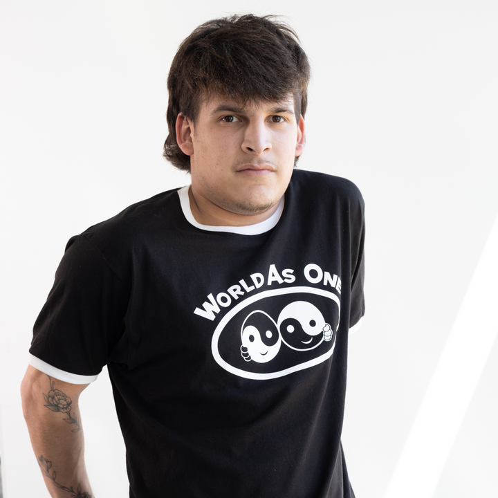 Man wearing a black t-shirt with a logo and text, sitting on a chair indoors.